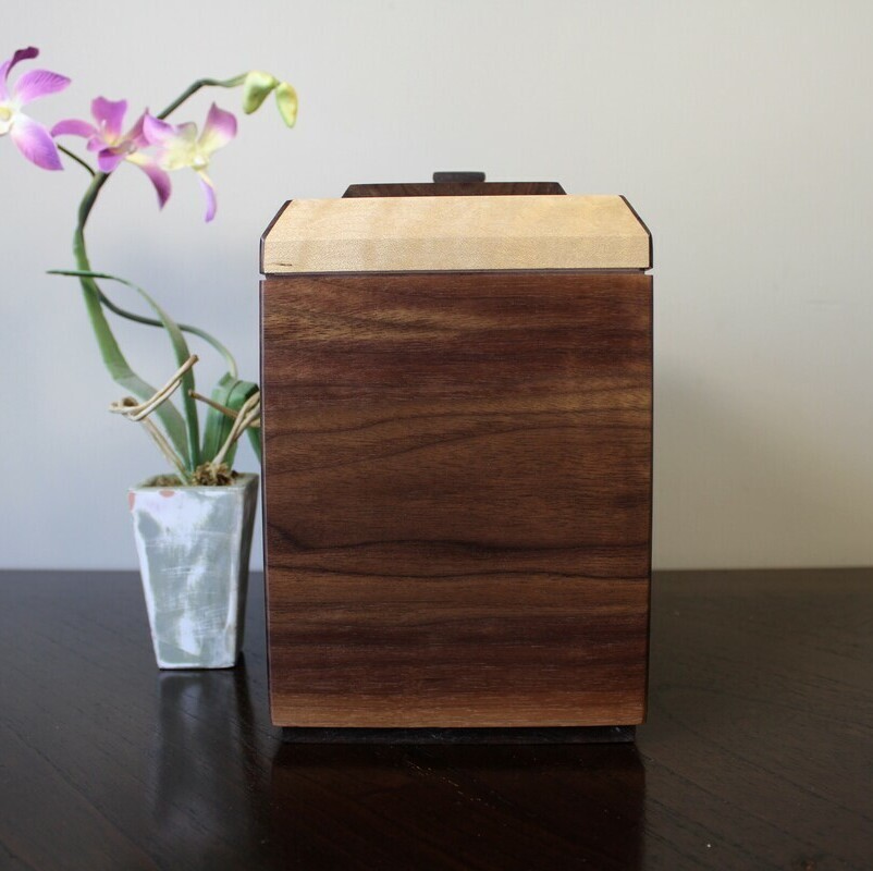 Left side view of a black walnut and figured maple wooden cremation urn with keepsake compartment