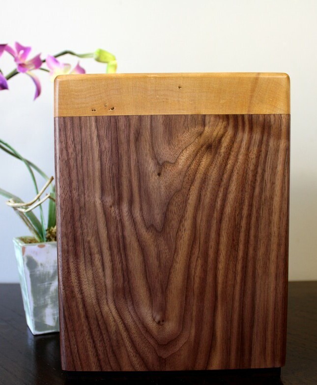 Front view of a black walnut and figured maple wooden cremation urn