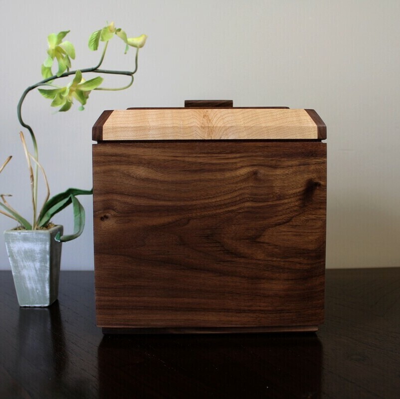 Front view of a black walnut and figured maple wooden cremation urn with integrated compartment 