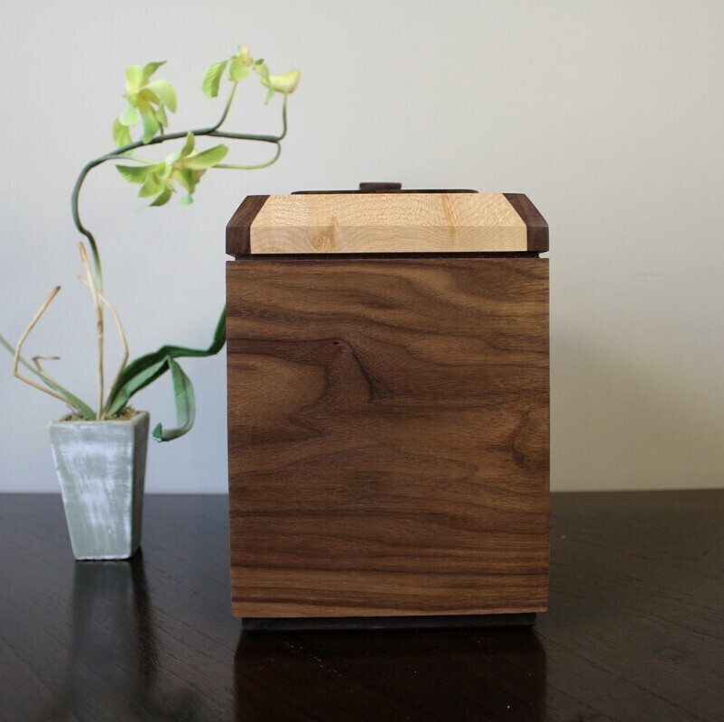 Left side view of a black walnut and figured maple wooden cremation urn with integrated compartment 