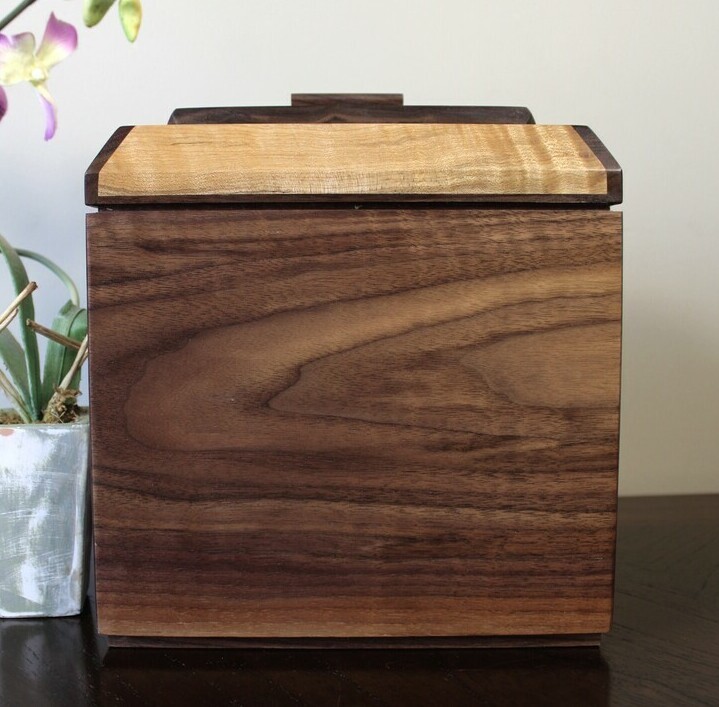 Front view of a black walnut and figured maple wooden cremation urn with receptacle
