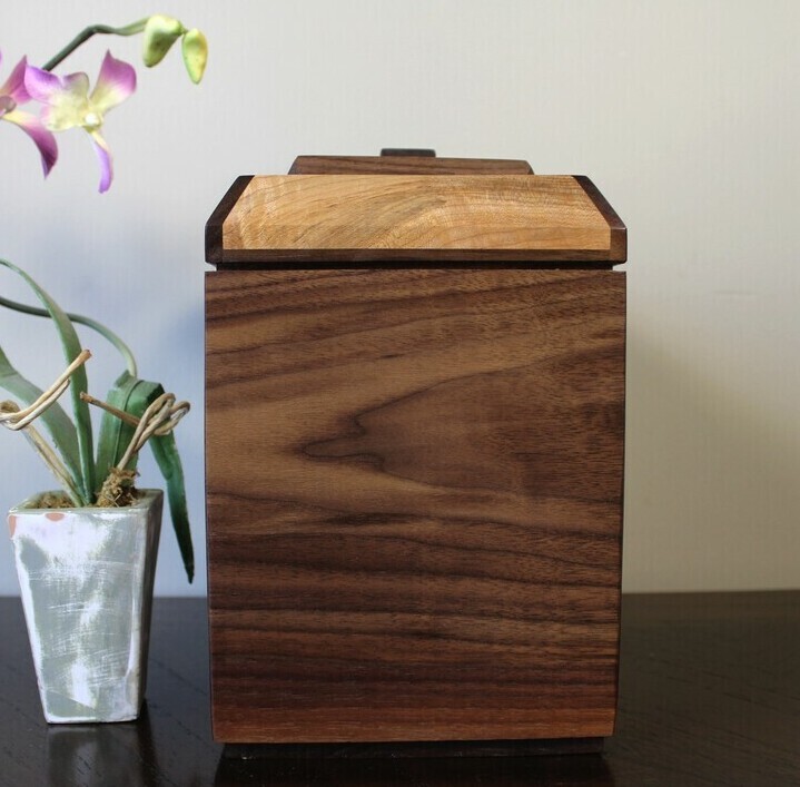 Left view of a black walnut and figured maple wooden cremation urn with receptacle