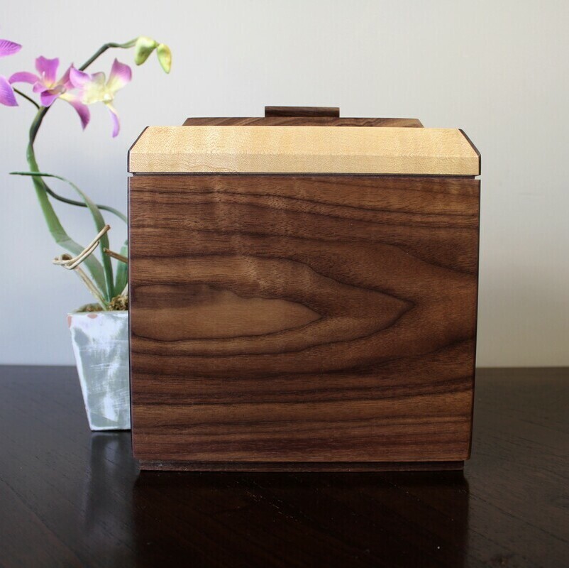 Back view of a black walnut and figured maple wooden cremation urn with keepsake compartment