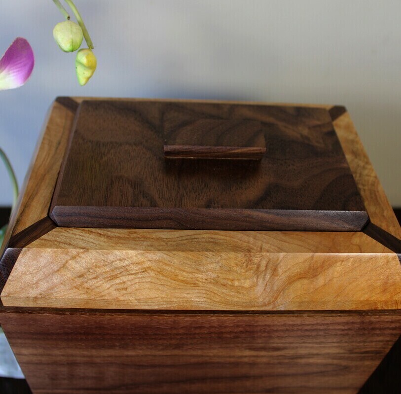 Top view of a black walnut and figured maple wooden cremation urn with receptacle