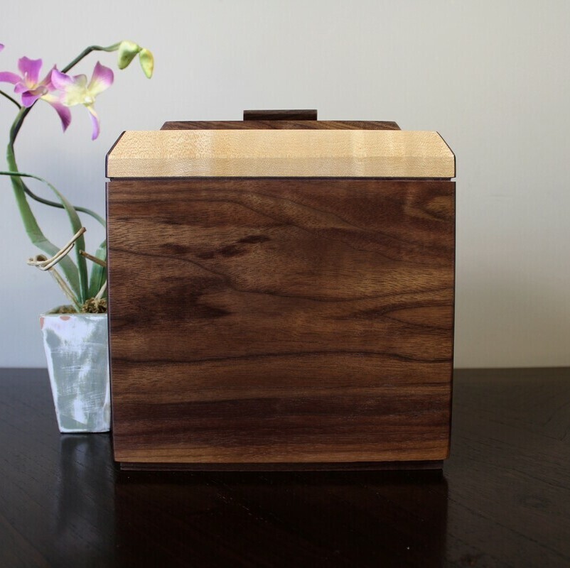 Front view of a black walnut and figured maple wooden cremation urn with keepsake compartment