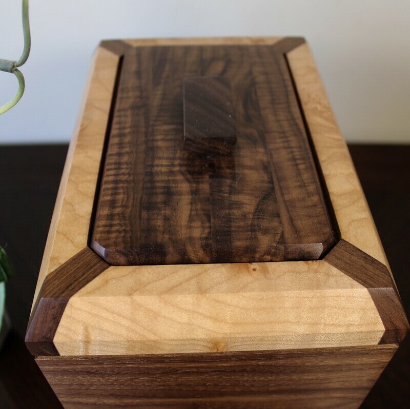 Compartment lid view of a black walnut and figured maple wooden cremation urn with integrated compartment 
