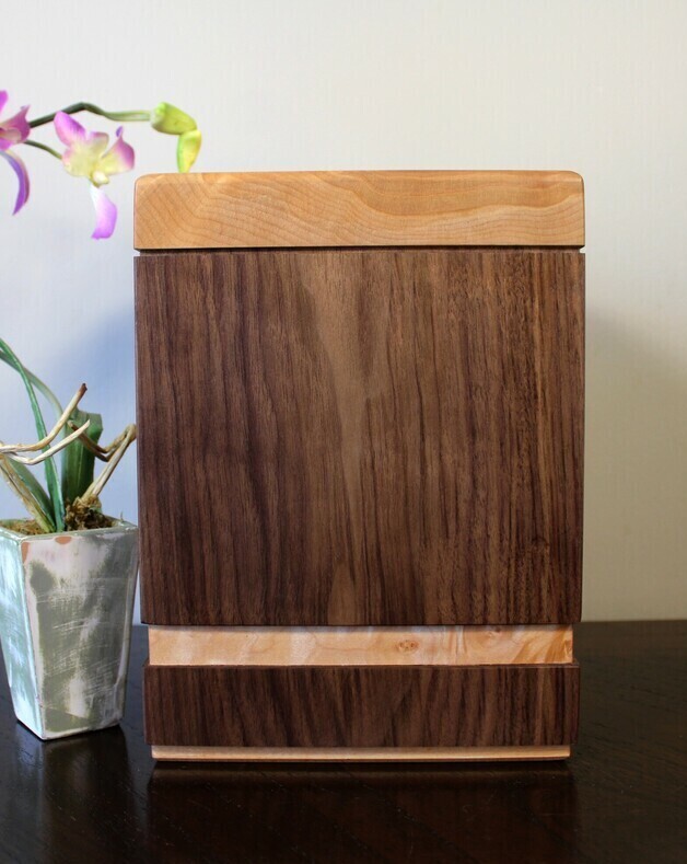 Left side view of a black walnut and quilted maple wooden cremation urn