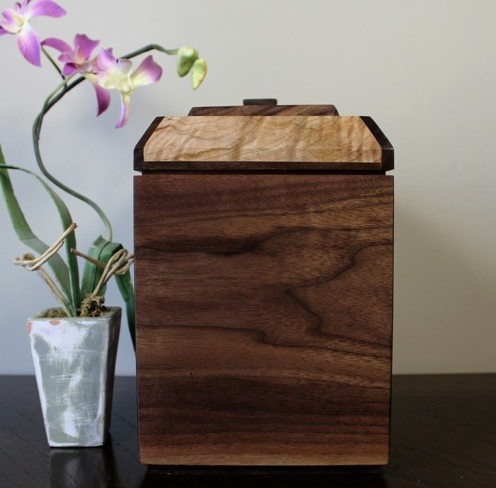 Right side view of a black walnut and figured maple wooden cremation urn with receptacle